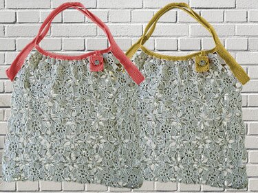 Zwei handgehäkelte Taschen aus hellgrauem Garn mit Blumen‑Lochmuster, eine mit korallenfarbenen, die andere mit senfgelben Henkeln, beide mit Knopfverschluss.