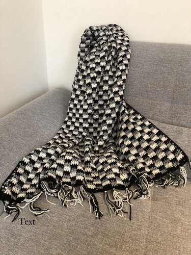Gehäkelte Decke in Schwarz, Weiß und Grau mit geometrischem Karomuster und Fransen auf grauem Sofa
