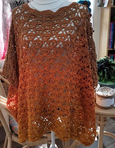 Gehäkelter braun-orangener Damenponcho mit Muschelmuster auf Schaufensterpuppe