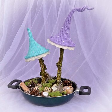 Gehäkelte Pilzhüte in Pastell auf Ästen mit Moos, Zapfen, Deko-Eiern und einem Stein mit 'Glück', arrangiert in einer Pfanne