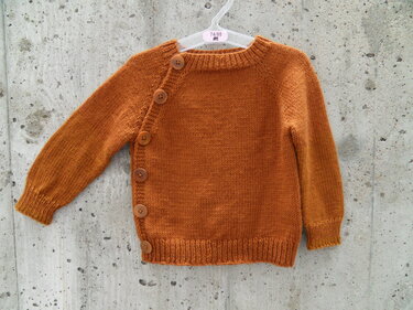 Rostbraune gestrickte Babyjacke mit seitlicher Knopfleiste, aufgehängt