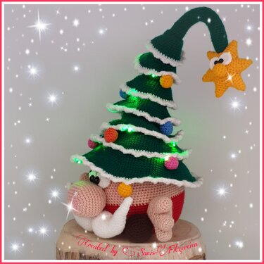 Gehäkelter Weihnachtswichtel in Tannenbaumform mit grünen LED-Lichtern und gelbem Stern auf Holzscheit