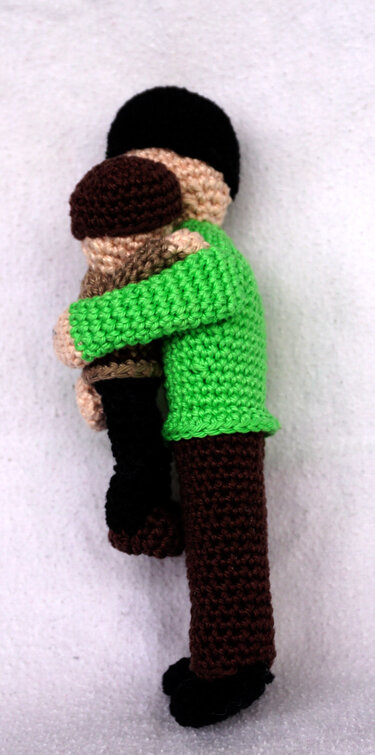 Zwei gehäkelte Amigurumi-Figuren umarmen sich, eine mit grünem Oberteil und braunen Hosen