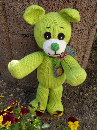 Grüner gestrickter Amigurumi-Teddy mit weißer Schnauze, grünem Näschen und Patch mit Knopf und Blüte