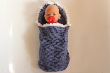 Babypuppe mit rotem Schnuller in blau-weißem, gehäkelten Schlafsack