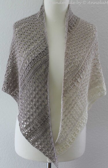 Crochet triangle shawl with an ombre lace pattern from light grey to cream, draped on a mannequin.