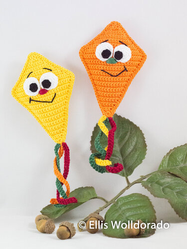 Zwei gehäkelte Deko‑Drachen in Gelb und Orange mit bunten, verdrehten Schweifen und freundlichen Gesichtern