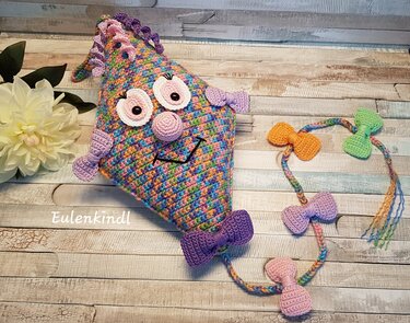 Gehäkelter bunter Amigurumi-Drachen mit Schleifen und geflochtenem Schwanz auf Holzhintergrund