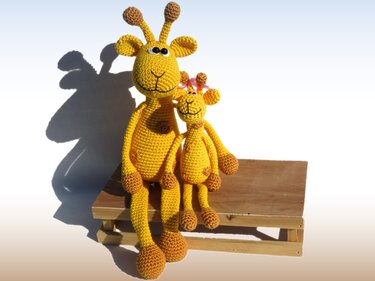 Große und kleine gelb-braune Amigurumi-Giraffen auf einem Holzhocker
