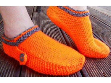 Gestrickte orange Hausschuhe mit grauem Rand und Knopf auf Holzterrasse