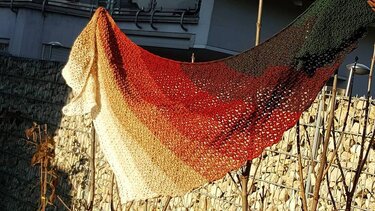 Gehäkeltes Dreieckstuch mit Farbverlauf in Beige, Rostrot und Dunkelgrün, im Sonnenlicht aufgehängt