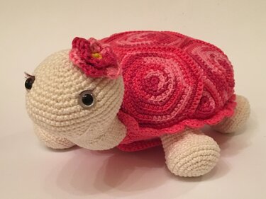 Amigurumi crochet turtle plush with a pink spiral shell and a small pink flower on its head.