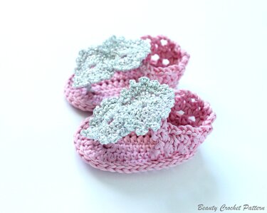 Rosa gehäkelte Babyschuhe mit silbernen Blättern auf hellem Hintergrund