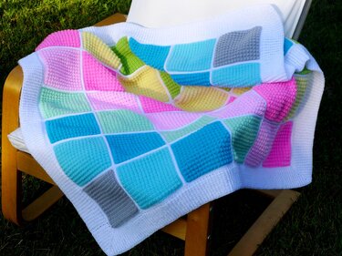 Crochet patchwork blanket of pastel textured squares with white border draped on a wooden chair