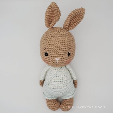 Beiger gehäkelter Amigurumi-Hase mit hellblauem Strampler vor hellem Hintergrund