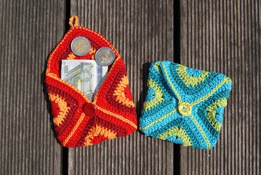 Gehäkelte Täschchen rot und blau-grün mit Münzen und Schein auf Holzdielen