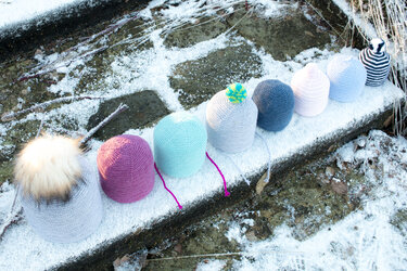 Verschiedene gestrickte Beanies und Bommelmützen liegen auf einer leicht verschneiten Fläche