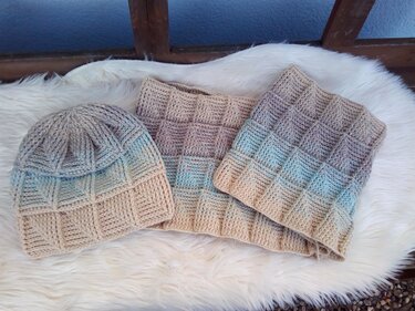 Gehäkeltes Damen-Set: Mütze und zwei Loops in Beige bis Hellblau mit kästchenartiger Reliefstruktur auf hellem Fell