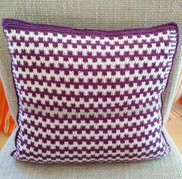 Quadratisches gestricktes Kissen mit lila-weißem Hahnentrittmuster auf beigem Sessel