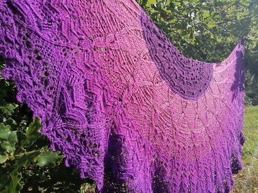 Detailaufnahme eines halbrunden gehäkelten Tuchs mit verschiedenen Spitzenmustern und gezacktem Rand in Violett- bis Rosatönen