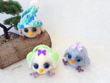 Drei gehäkelte Amigurumi-Vögel: einer mit blau-weiß gestreifter Bommelmütze, einer mit grünen Ohrenschützern und lila Schleife, einer mit rosa Schleife.