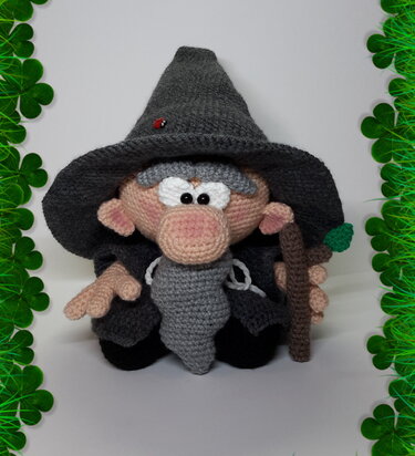 Gehäkelter Amigurumi-Zauberer mit spitzem Hut, Bart, Stab und Marienkäfer vor kleeblattförmigem Rahmen