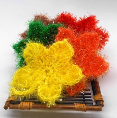 Gehäkelte, flauschige Blumen in mehreren Farben mit einer kleinen Aufhängeschlaufe auf einem Tablett