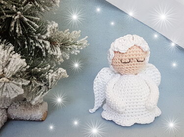 Weißer gehäkelter Amigurumi-Engel mit Flügeln neben beschneitem Tannenbaum