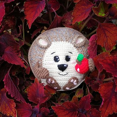 Runder gehäkelter Igel mit rotem Apfel und sichtbaren Maschen