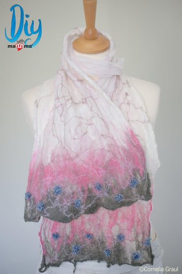 Filzschal mit Farbverlauf (weiß-pink-grau) und blauen Blumen auf einer Schneiderpuppe.