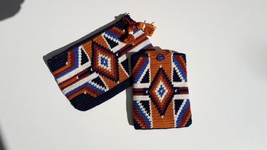 Zwei gehäkelte Taschen im geometrischen Rautenmuster (Dunkelblau, Orange, Weiß, Rostbraun): eine Clutch mit Reißverschluss und Quasten und eine schmalere Hülle mit Knopf.