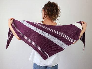 Person hält ausgebreitetes gestricktes Dreieckstuch in Pflaume mit hellgrauem Zopf und weißen Streifen