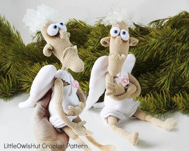 Two crochet amigurumi angels with looped curly hair, white wings and outfits; one held by a hand for scale against an evergreen background