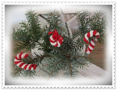 Drei gehäkelte rot-weiße Weihnachtsanhänger in Zuckerstangen- und Spiralform an Tannenzweigen