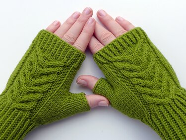 Hands wearing green fingerless knitted gloves with a leaf cable pattern and ribbed cuffs