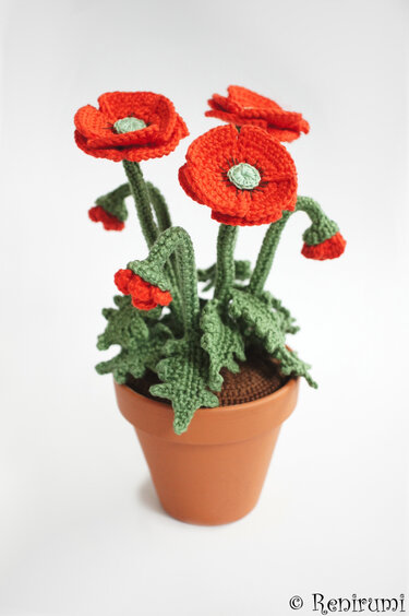 Crocheted red poppies and green leaves in a terracotta pot showing stitch detail for a pattern