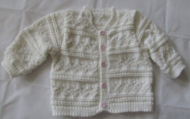 Weiße gestrickte Babyjacke mit Rundhalsausschnitt und fünf rosa Knöpfen