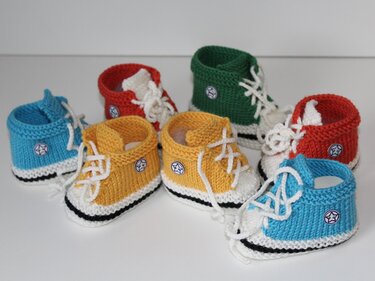 Mehrere gestrickte Babyschuhe im Sneaker-Stil in Blau, Gelb, Rot und Grün mit weißen Schnürsenkeln