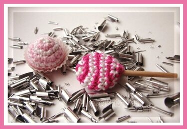 Gehäkeltes Bonbon im Förmchen und gestreifter Lutscher in Rosa und Weiß auf silberner Streudeko.
