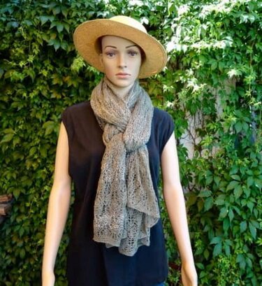 Schaufensterpuppe mit beigem gestricktem Lacetuch im Lace-Muster und Strohhut vor grüner Hecke