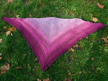 Gehäkeltes dreieckiges Tuch in Rosa- und Magentatönen mit Ajourmuster, liegend auf Gras