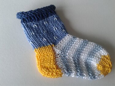 Small knitted baby sock with variegated blue-and-white foot, yellow heel and toe, and dark blue rolled cuff