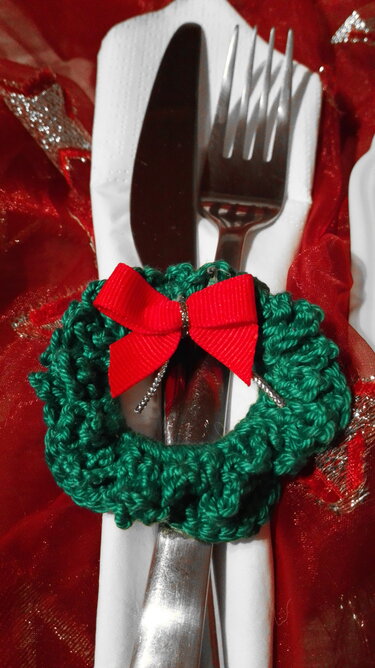 Besteck mit gehäkeltem grünen Mini-Weihnachtskranz und roter Schleife auf rotem Stoff