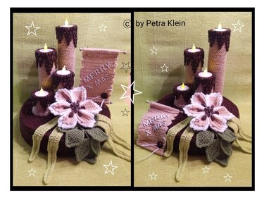 Gehäkeltes Adventsarrangement mit vier Kerzen in Beige und Dunkelbraun, rosa Blüte, grünen Blättern und Banner mit der Aufschrift 'MERRY X MAS'.