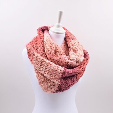 Variegated pink, peach, and burgundy crocheted infinity scarf with an open textured stitch, shown on a white mannequin torso.