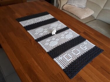 Gehäkelter Tischläufer in Grau und Weiß mit Streifen- und Herzmuster auf Holztisch.