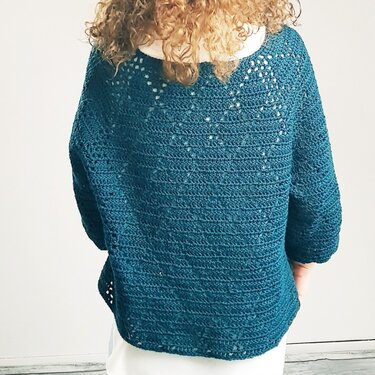 Back view of a woman wearing a teal crocheted sweater with a lacy yoke.