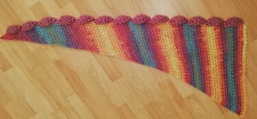 Gehäkelter Drachenschwanz-Schal, Regenbogen-Farbverlauf, Glitzereffekt und rosa Noppenkante auf Holzboden