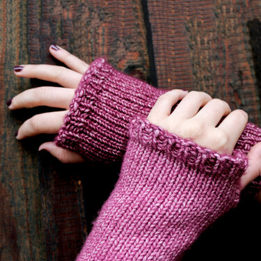 Nahaufnahme mauvefarbener, gestrickter fingerloser Armstulpen an Händen auf Holzhintergrund
