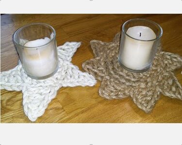 Zwei gehäkelte sternförmige Untersetzer, einer weiß, einer braun, jeweils mit einem Kerzenglas auf einem Holztisch.